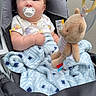 baby, infant, child, stroller, pacifier, teddy_bear, blanket, plush_toy, sitting, portrait, wide_eyed, brown_hair, clothing, outdoor, daylight, cozy, baby_gear, toy, fabric, closeup