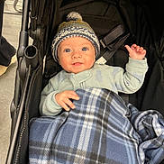 Bennett joined the competition — help win amazing prizes! baby, child, stroller, blanket, hat, knit_hat, plaid, blue, smile, face, person, clothing, baby_clothes, indoor, infant, cute, warm, cozy, hand, seatbelt