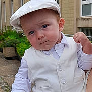 Maël a rejoint le concours — aidez-le/la à gagner de superbes lots ! baby, child, white_clothing, vest, cap, blue_eyes, outdoor, building, hand, smartphone, person, expression, portrait, fashion, cute, serious, holding, adult_hand, garden, sidewalk