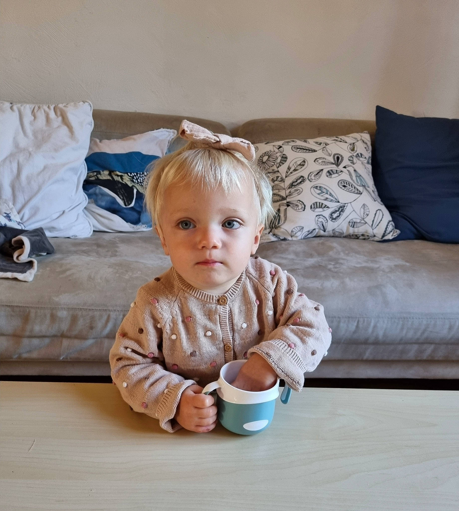 Hanna participe au concours pour gagner de l'argent avec cette photo : baby, baby_toddler_clothing, child, comfort, couch, drinkware, face, floor, flooring, hardwood, living_room, person, serveware, sitting, sleeve, studio_couch, table, tableware, toddler, wood
