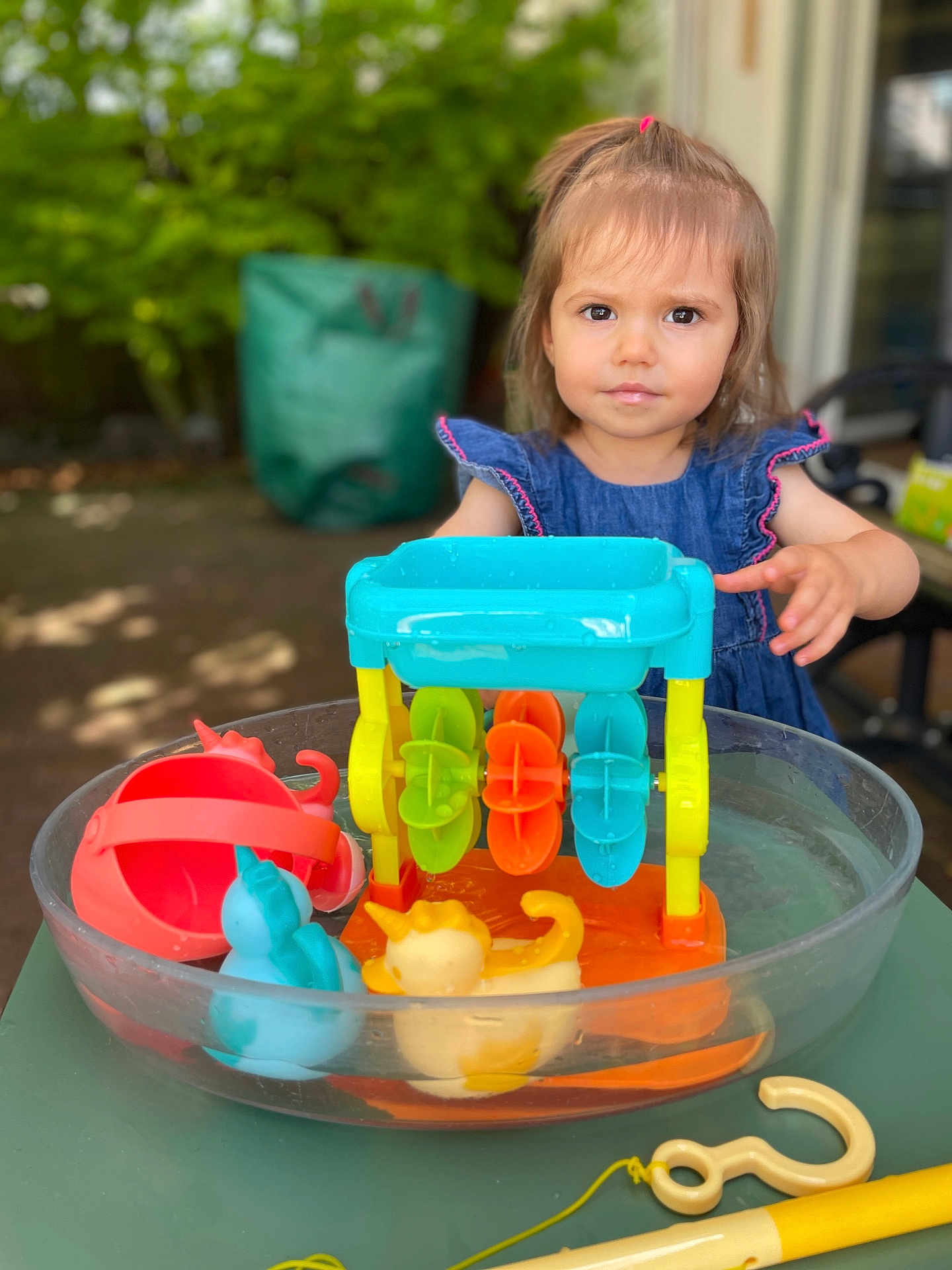 Mya a rejoint le concours — aidez-le/la à gagner de superbes lots ! toddler, child, toy, water, plastic_basin, outdoor, greenery, denim_dress, play, colorful, yellow, blue, orange, red, summer, daylight, curious, face, person, young
