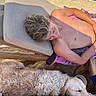 boy, shirtless, relaxing, beach_chair, dog, golden_retriever, sleeping, sand, outdoor, sunlight, vacation, summer, resting, wooden_furniture, towel, pet, animal, human, leisure, daytime