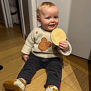 Lucas Bequin participe au concours pour gagner de l'argent avec cette photo : baby, child, sitting, floor, wooden_floor, sweater, mickey_mouse, plush_chair, doorway, pants, socks, shoes, holding, wooden_plaque, indoor, smiling, cute, happy, person, portrait