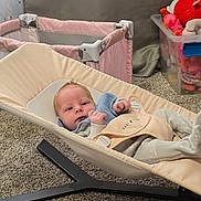 Sawyer joined the competition — help win amazing prizes! baby, infant, baby_bouncer, baby_seat, pink_playpen, toys, plush_toy, storage_box, carpet, nursery, bib, strap, buckle, clothing, face, gaze, newborn, cozy, home_interior, beige_fabric