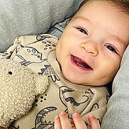 Zayn a rejoint le concours — aidez-le/la à gagner de superbes lots ! baby, smile, teddy_bear, cuddly_toy, dinosaur_print, cute, child, happy, infant, clothing, hand, face, portrait, cozy, soft_texture, fabric, close_up, young_child, indoor, light