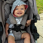 Malak is registered to the contest to win money with this photo: toddler, child, stroller, baby, smiling, hood, shark_costume, blue_eyes, outdoor, grass, socks, seatbelt, happy, cute, infant, casual_clothing, fabric, baby_wear, playful, person