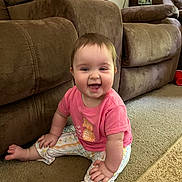 Lilia joined the competition — help win amazing prizes! baby, child, smiling, sitting, pink_shirt, patterned_pants, carpet, couch, furniture, indoor, living_room, happy, person, face, footwear_free, cute, young_child, home, playful, infant