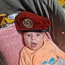 baby, badge, beret, blanket, car_seat, child, clothing, eyes, face, hat, indoor, infant, metal_emblem, onesie, pacifier_clip, pink_towel, plush_toy, portrait, surprised, tongue_out