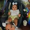 baby, infant, car_seat, bow, reflection, blur, bottle, clothing, green, white, face, child, seated, indoor, cute, portrait, soft_light, toy, daisy_pattern, bib