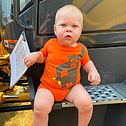 Alidar joined the competition — help win amazing prizes! baby, child, infant, construction_vehicle, excavator, orange_clothing, romper, sitting, face, portrait, blue_eyes, blond_hair, outdoor, machinery, vehicle, metal_step, paperwork, warning_label, grass, sunlight