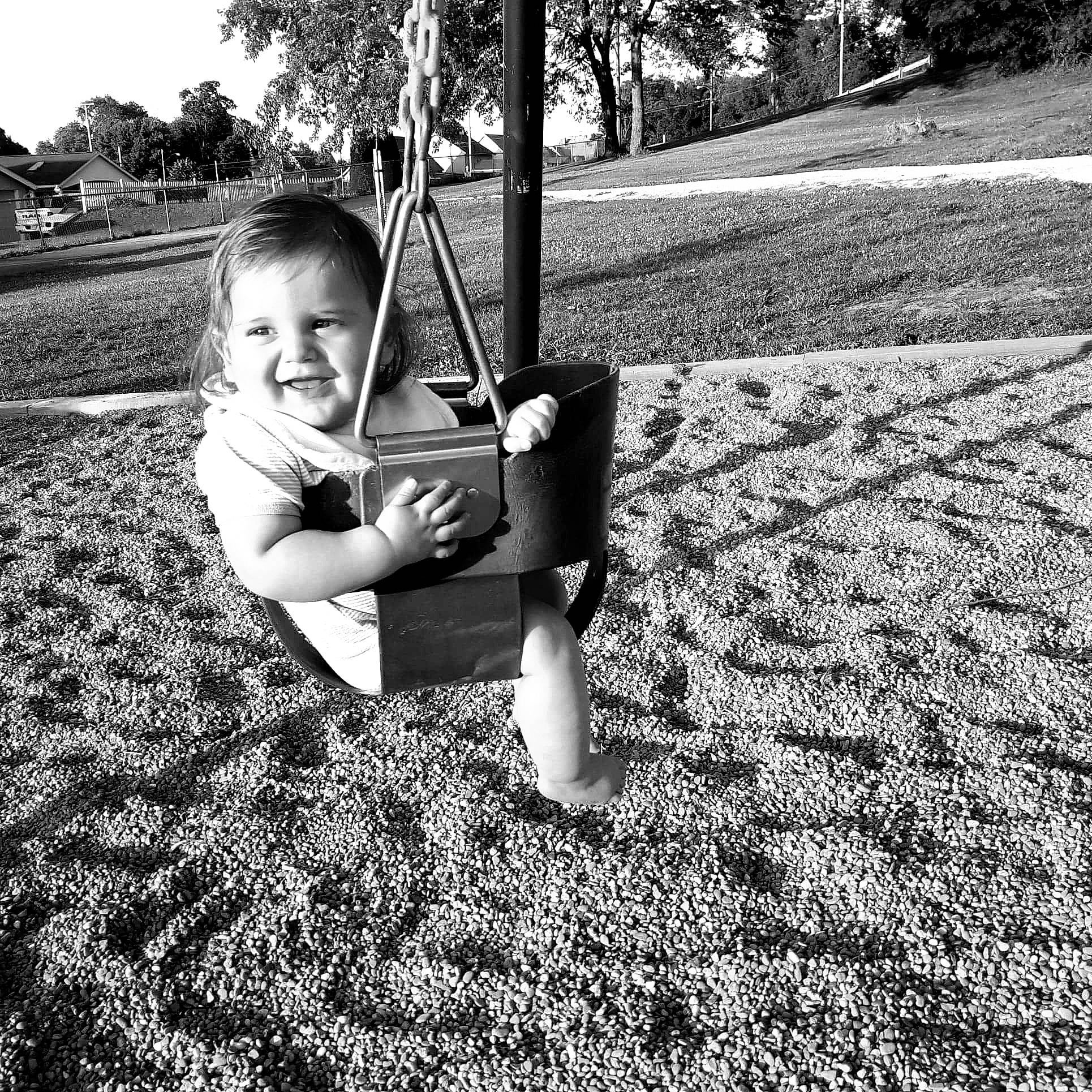 Thatcher is registered to the contest to win money with this photo: black, black_and_white, child, fun, grass, joy, monochrome, monochrome_photography, outdoor_play_equipment, person, photography, plant, play, playground, public_space, snapshot, stock_photography, swing, toddler, tree
