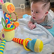 Nathan is registered to the contest to win money with this photo: baby, child, infant, tummy_time, curious, looking, face, eyes, hair, smiling_toy, plush_toy, caterpillar, rattle, blanket, bed, indoor, home, wood_floor, colorful, portrait
