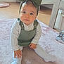 baby, child, headband, green_bow, carpet, indoor, crawling, cute, blue_eyes, white_sweater, green_overalls, nursery, wooden_furniture, soft_lighting, floor, toddler, person, home, playroom, sitting