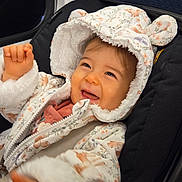Margot participe au concours pour gagner de l'argent avec cette photo : baby, child, smiling, hood, jacket, car_seat, cute, happy, clothing, infant, seatbelt, indoor, person, face, expression, warm_clothing, fur_trim, joy, small_hands, transportation