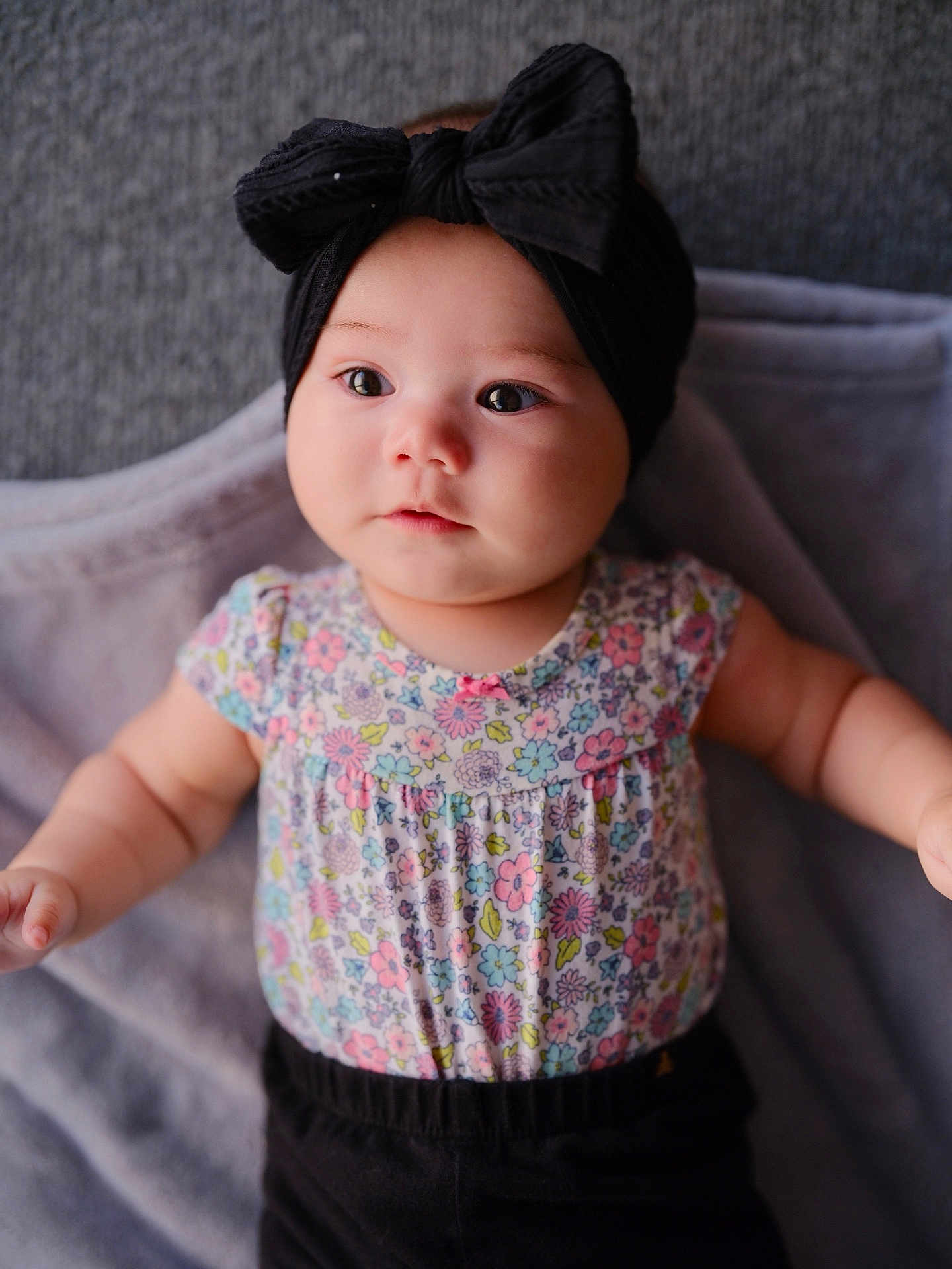Ava Angeline is registered to the contest to win money with this photo: baby, infant, headband, bow, floral_clothing, blanket, portrait, cute, chubby_cheeks, soft_lighting, indoors, child, expression, skin, black_pants, person, closeup, adorable, young_child, lying_down