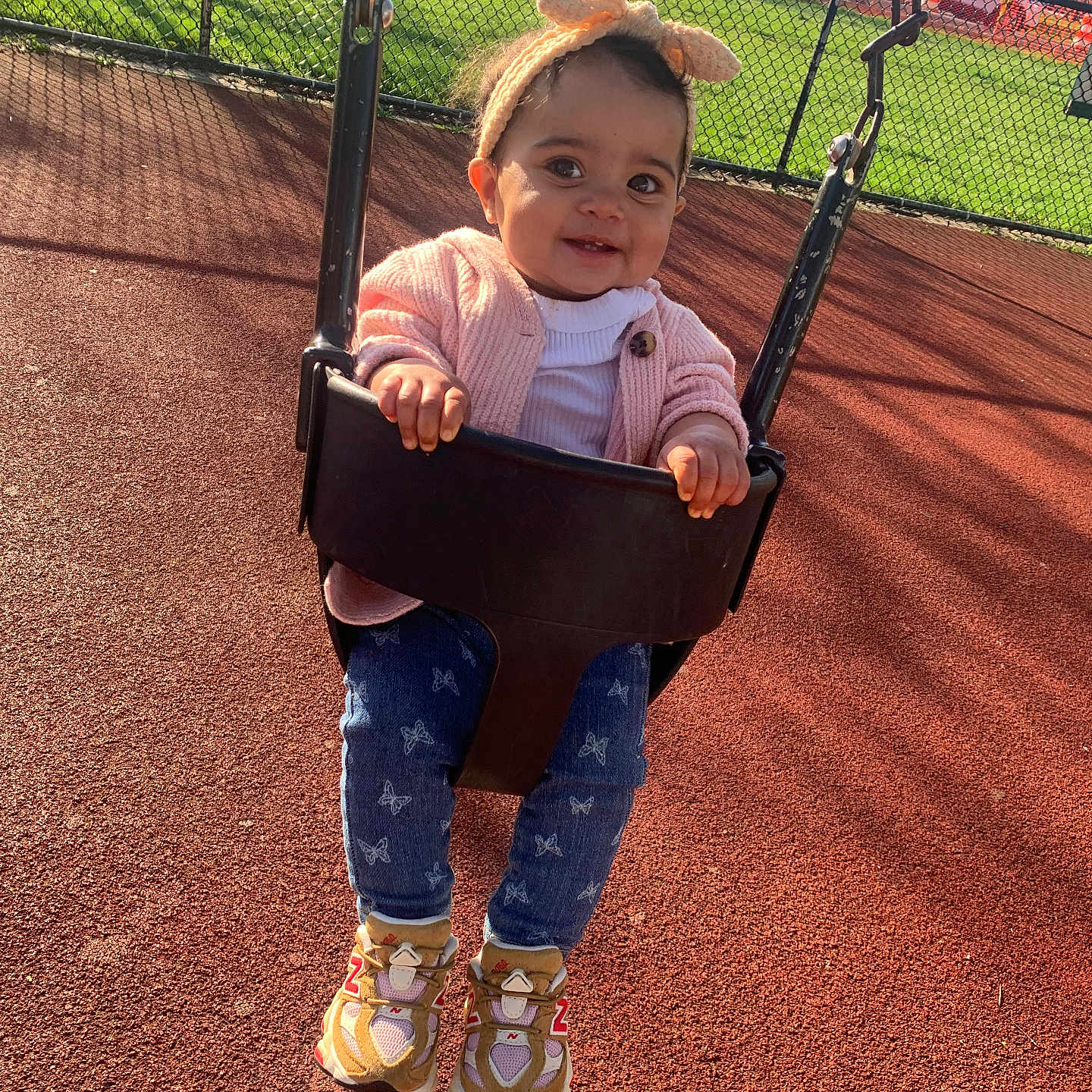 Kazora joined the competition — help win amazing prizes! baby, bow, butterfly_print, chain_link_fence, child, daytime, fun, grass, happy, headband, jeans, outdoor, pink_cardigan, play_area, playground, smiling, sneakers, sunny, swing, toddler