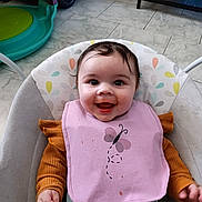 Rose participe au concours pour gagner de l'argent avec cette photo : baby, infant, smile, bib, feeding_bib, bouncer, seat, highchair, happy, face, eyes, cheeks, food_smear, clothing, patterned_cushion, tile_floor, toy_car, play_area, hands, indoor