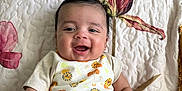 Dylan is registered to the contest to win money with this photo: baby, smiling, infant, onesie, lion_pattern, quilted_blanket, floral, happy, cute, child, portrait, indoor, skin, hand, face, sitting, young_child, short_hair, comfortable, bright