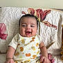 baby, smiling, infant, onesie, lion_pattern, quilted_blanket, floral, happy, cute, child, portrait, indoor, skin, hand, face, sitting, young_child, short_hair, comfortable, bright