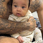 Jovani joined the competition — help win amazing prizes! baby, infant, tattoos, arms, pajamas, clothing, person, skin, face, eyes, expression, hand, legs, indoors, bedroom, blurred_background, holding, cute, young_child, closeup