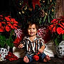 barefoot, child, christmas_decor, cute, decorative_pillow, festive, gift_wrapping, greenery, holiday, indoor, jeans, poinsettia, red_flowers, red_jingle_bell, sitting, smile, snowflake, striped_shirt, toddler, wooden_floor