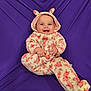 baby, baby_clothes, child, cozy, cute, expression, face, floral_pattern, happy, headwear, hooded_clothing, indoor, infant, onesie, person, playful, portrait, purple_background, sitting, smiling