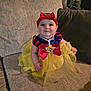 Suriya is registered to the contest to win money with this photo: baby, child, costume, dress, red_bow, yellow_tutu, couch, smile, indoor, headband, person, cute, happy, sitting, plush, infant, face, eyes, cheeks, portrait