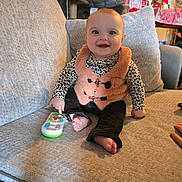 Suriya joined the competition — help win amazing prizes! baby, child, smiling, sitting, couch, toy, remote_control, clothing, orange_vest, leopard_print, barefoot, indoor, home, holiday_decor, festive, pillow, happy, person, infant, furniture