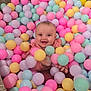 Suriya is registered to the contest to win money with this photo: baby, child, ball_pit, colorful_balls, pastel_colors, happy, smiling, playful, indoor, carpet, pink, yellow, blue, purple, cute, infant, joy, fun, sitting, person