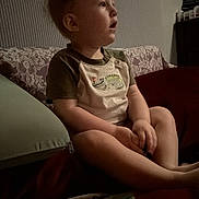 Thomas is registered to the contest to win money with this photo: child, toddler, baby, sitting, couch, sofa, portrait, profile, face, indoor, home, clothing, short_sleeves, pillow, blanket, toy, colorful, curious, dim_lighting, family