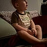 child, toddler, baby, sitting, couch, sofa, portrait, profile, face, indoor, home, clothing, short_sleeves, pillow, blanket, toy, colorful, curious, dim_lighting, family
