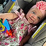 baby, child, car_seat, pink_dress, headband, flower, toy, smile, blue_eyes, rosy_cheeks, infant, cute, happy, seated, colorful, plastic_rings, fabric, pattern, ribbon, portrait