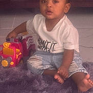 Nathan is registered to the contest to win money with this photo: child, toddler, toy_truck, purple_rug, indoor, floor, white_tshirt, denim_shorts, barefoot, curious, sitting, young_child, home, playtime, casual_clothing, expression, person, cute, baby, car_toy