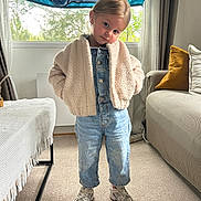 Abby a rejoint le concours — aidez-le/la à gagner de superbes lots ! child, indoor, standing, jacket, denim, overalls, sneakers, carpet, couch, pillow, window, blanket, curtains, natural_light, person, confident_pose, living_room, floor, cute, smiling
