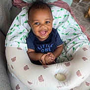 Ayden is registered to the contest to win money with this photo: baby, infant, smiling, happy, child, indoor, inflatable_ring, bear_pattern, clothing, blue_shirt, wild_hair, person, cute, seated, toddler, blanket, fabric, home, playful, joyful