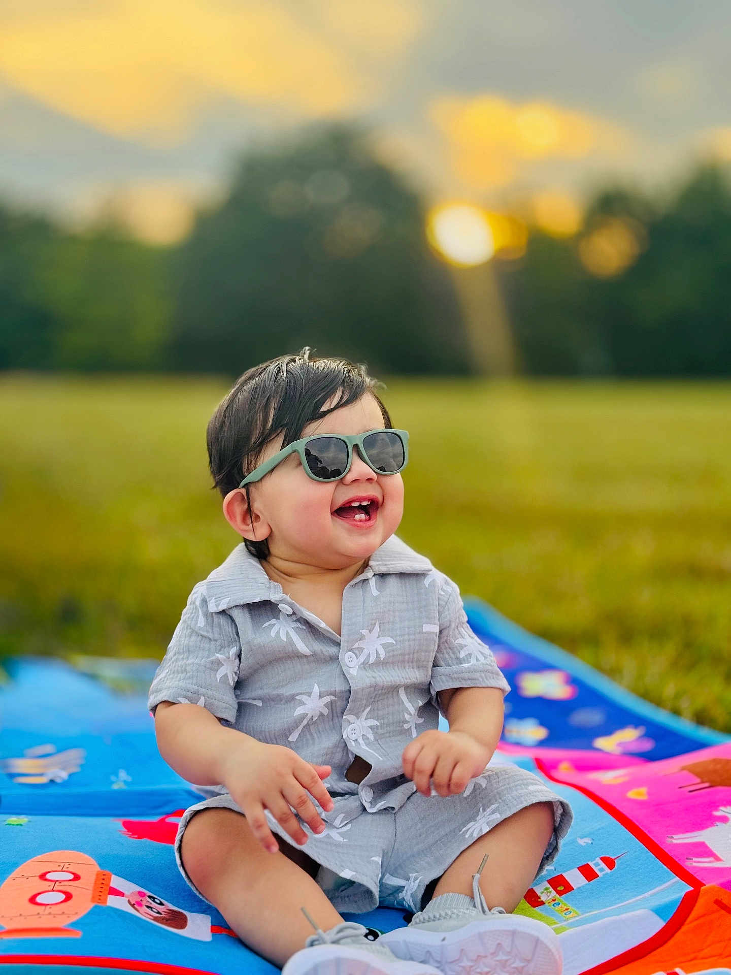 Arshan joined the competition — help win amazing prizes! toddler, child, sunglasses, smiling, outdoor, grass, blanket, summer_clothing, happy, baby, field, nature, sunset, casual, cute, sitting, portrait, daylight, playful, fun