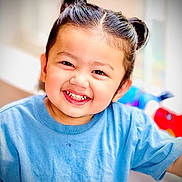 Arshan joined the competition — help win amazing prizes! child, smiling, portrait, indoors, blue_shirt, double_bun, dark_hair, happy, teeth, face, head, person, close_up, looking_at_camera, colorful_background, toys, casual_clothing, sitting, bright_lighting, photography