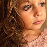child, girl, portrait, close_up, face, curly_hair, brown_hair, blue_eyes, looking_away, serious_expression, pink_dress, sequins, sparkles, shoulders, indoor, warm_lighting, photography, beauty, young_person, fashion