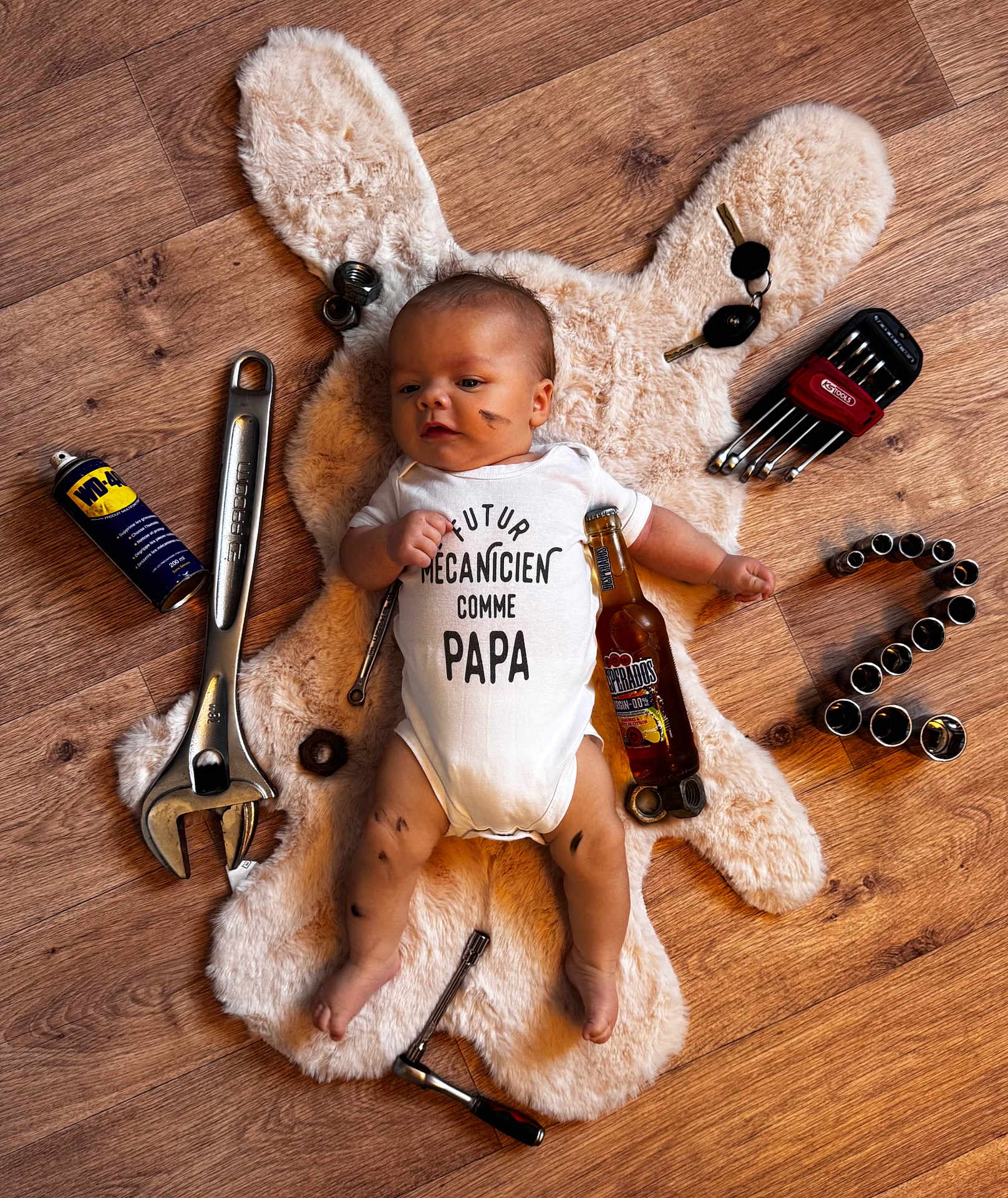 Loan a rejoint le concours — aidez-le/la à gagner de superbes lots ! baby, infant, onesie, floor, wooden_floor, tools, wrench, ratchet, nuts, bolts, keys, beer_bottle, plush_rug, face_smudge, legs_smudge, cute, lying_down, mechanic_theme, child, indoors