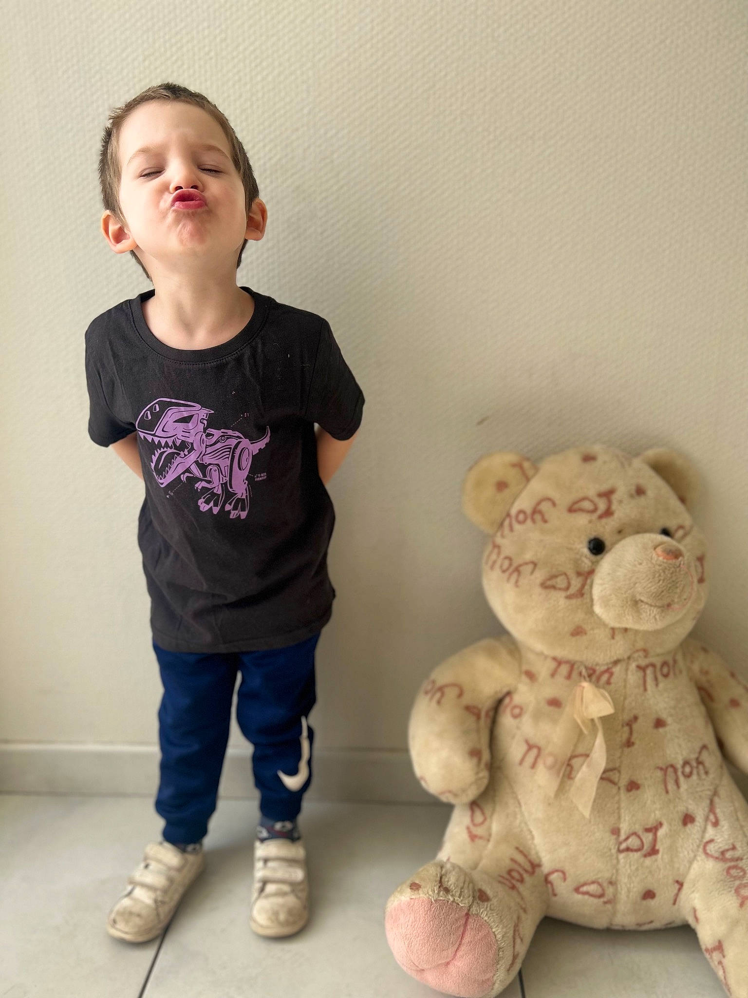 Kelyan participe au concours pour gagner de l'argent avec cette photo : cheek, child, chin, felidae, happy, human_body, human_leg, knee, nose, person, pink, room, skin, sleeve, snout, standing, stuffed_toy, t_shirt, teddy_bear, toddler