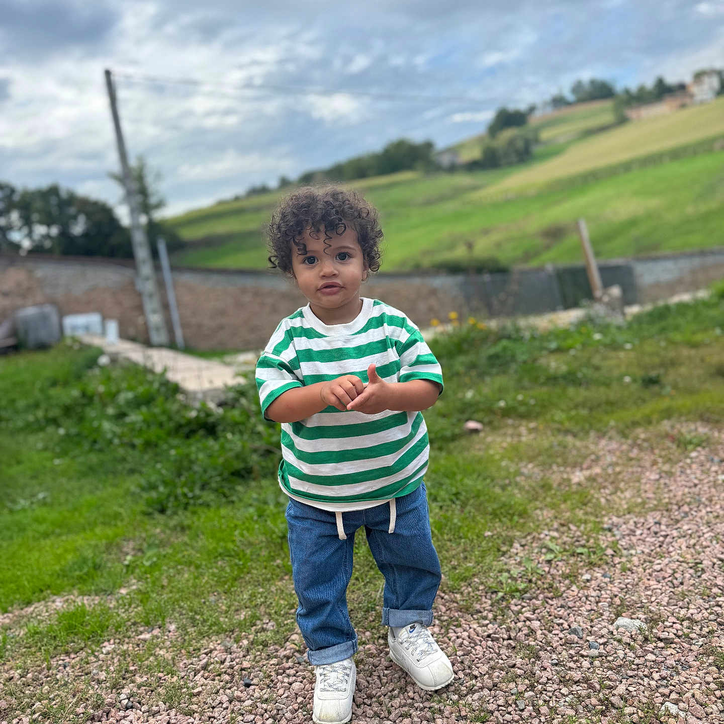 Khelis participe au concours pour gagner de l'argent avec cette photo : blue_jeans, casual_clothing, child, cloudy_sky, curly_hair, daylight, field, grass, gravel, green_shirt, nature, outdoor, person, portrait, rural, sky, standing, striped_shirt, toddler, white_sneakers