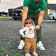 Ezequiel Cortinez is registered to the contest to win money with this photo: toddler, child, adult, walking, sunglasses, bear_shirt, green_shirt, green_pants, sandals, sneakers, gravel, outdoor, tree, car, supporting, holding_hands, casual_clothing, daylight, person, portrait