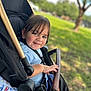 toddler, child, smile, stroller, outdoor, park, greenery, sunlight, baby, happy, seatbelt, hand, face, hair, nature, grass, tree, foot, casual_clothing, daytime