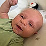 Freddie is registered to the contest to win money with this photo: baby, infant, face, smile, fist, green_clothing, onesie, cushion, star_pattern, plush_toy, penguin, skin, head, lying_down, cute, closeup, child, happy, indoors, person