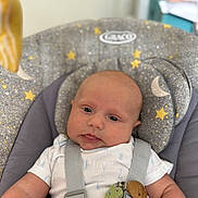Freddie is registered to the contest to win money with this photo: baby, infant, face, person, child, seat, baby_seat, straps, clothing, onesie, toy, cactus_toy, wooden_beads, head, skin, indoors, comfort, expression, closeup, cute