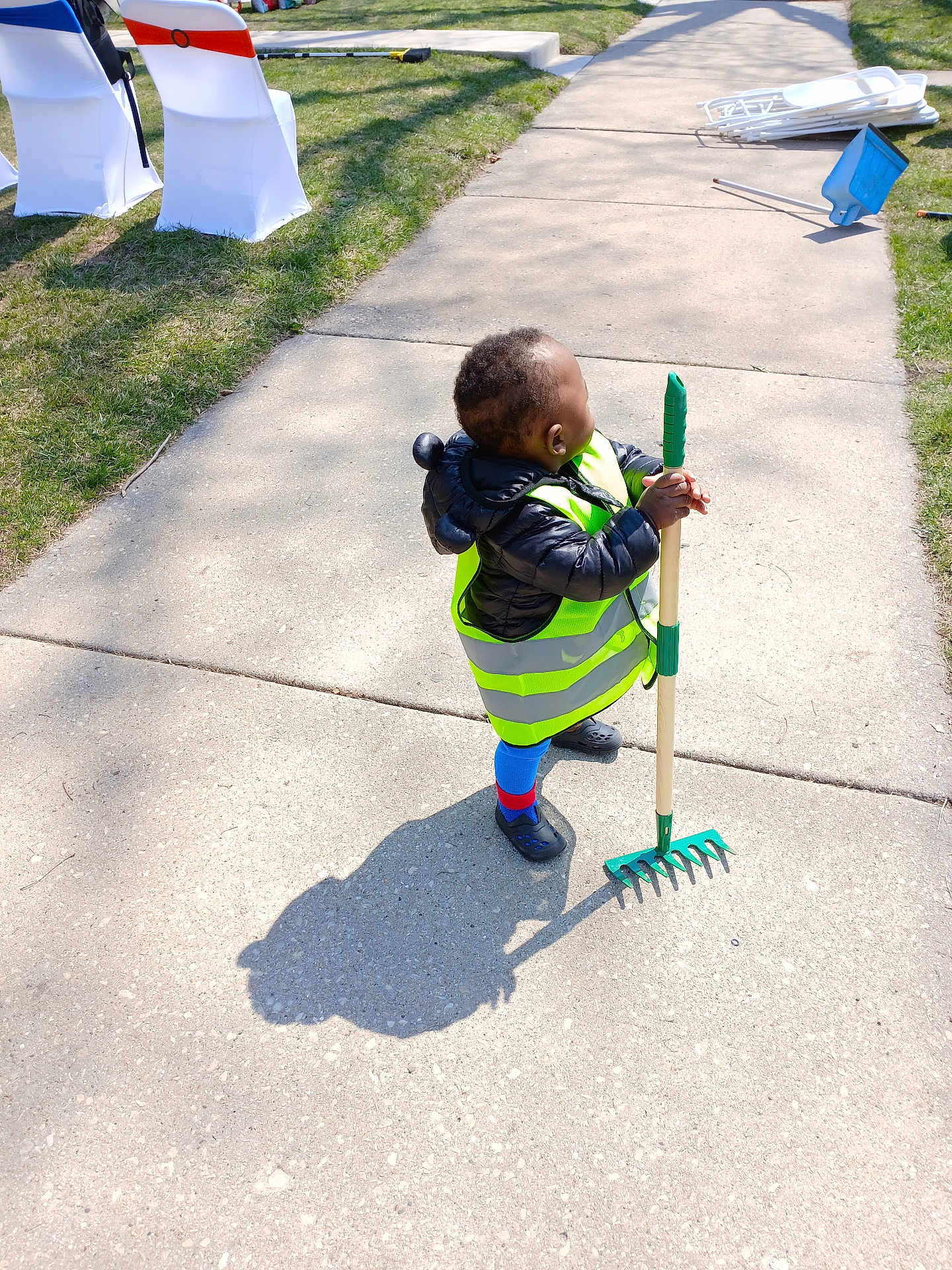 Jamar Leonard joined the competition — help win amazing prizes! child, sidewalk, grass, rake, shadow, jacket, reflective_vest, blue_socks, clogs, outdoor, daylight, sunlight, toy, yard_work, play, person, green, blue, concrete, small