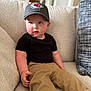 Canaan joined the competition — help win amazing prizes! toddler, child, person, couch, indoor, clothing, hat, cap, black_shirt, tan_pants, face, skin, furniture, seated, curious, blue_eyes, casual, home, portrait, relaxing