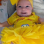 Peyton is registered to the contest to win money with this photo: baby, child, yellow_bow, yellow_dress, smiling, happy, infant, tutu, headwear, cute, soft_blanket, nursery, indoor, portrait, playful, clothing, sitting, closeup, adorable, face