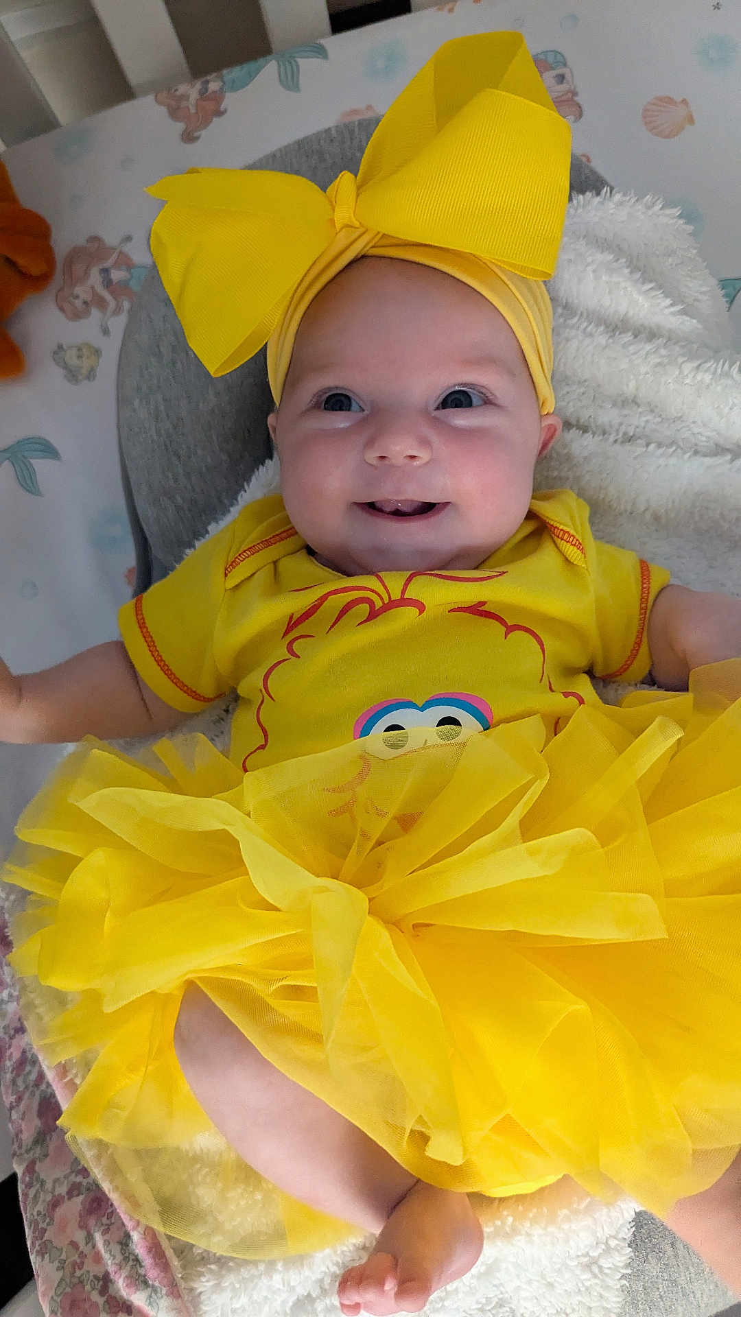 Peyton is registered to the contest to win money with this photo: baby, child, yellow_bow, yellow_dress, smiling, happy, infant, tutu, headwear, cute, soft_blanket, nursery, indoor, portrait, playful, clothing, sitting, closeup, adorable, face