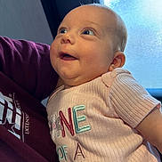 Rhilley is registered to the contest to win money with this photo: baby, infant, child, person, cute, smiling, looking_up, pink_shirt, embroidery, indoor, natural_light, window, adult_arm, maroon_shirt, portrait, happy, young_child, closeup, skin, face